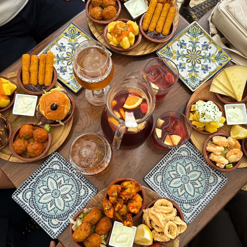 A table seen from above with clay dishes to share, a jug of sangria and glasses of beer, at our restaurant in Málaga’s old town